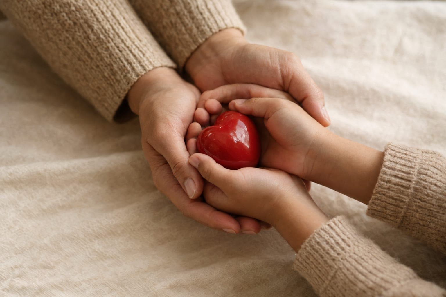 Manos de una mujer y de una niña sosteniendo juntas un corazón rojo